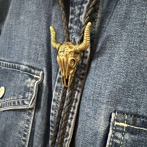 Antique gold tone steer skull bolo tie with black braided faux leather cord, adjustable slider pendant, and matching antique gold tips.