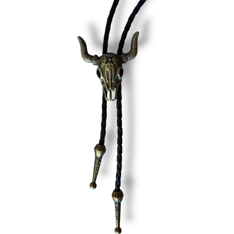 Antique gold tone steer skull bolo tie with black braided faux leather cord, adjustable slider pendant, and matching antique gold tips.