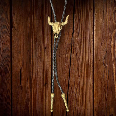 Antique gold steer skull bolo tie with adjustable slide and braided faux-leather rope. Unisex Western neckwear for concerts, festivals, and everyday edge.