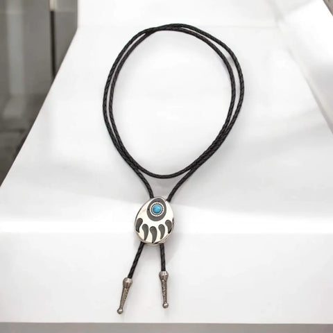 Two bear paw bolo ties with black braided leather cords: silver-tone faux turquoise bear claw slider and black stone bear paw pendant with antique metal tips.
