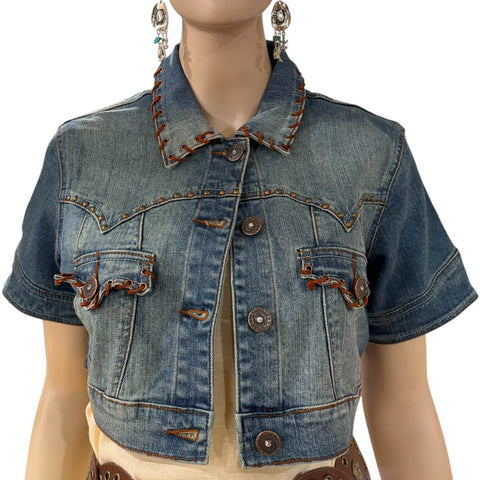Woman wearing short sleeve cropped jean jacket with leather lacing over a cream maxi dress