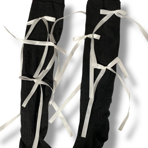 Woman wearing knee high socks with long satin bow ribbons, coquette balletcore legwear for cosplay, Y2K fashion, and festival outfits.
