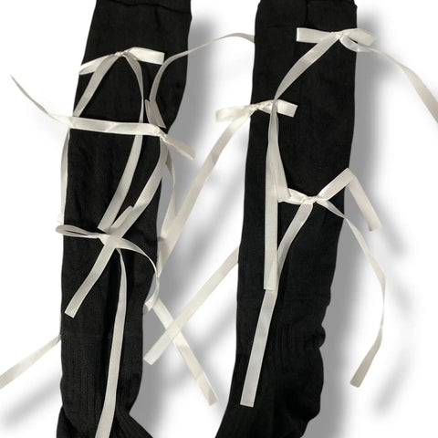Woman wearing knee high socks with long satin bow ribbons, coquette balletcore legwear for cosplay, Y2K fashion, and festival outfits.
