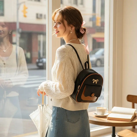 lifestyle woman shopping wearing Black Brown Trim Mini Backpack with gold bow detail and adjustable straps / one size