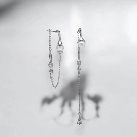 Silver asymmetrical pearl drop earrings with silver curb chains, simulated white pearls, and crystal accents, modern gothic and Y2K fashion jewelry.