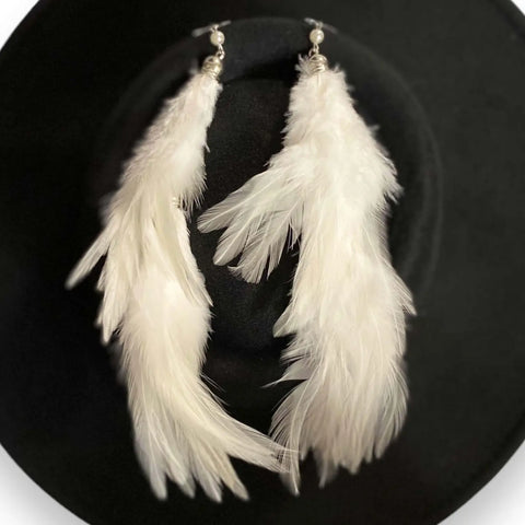 white natural feather tassel earrings on top of black round pork pie fedora hat